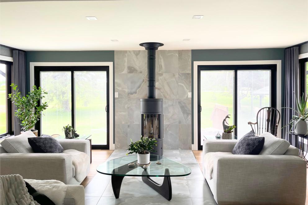 Sunroom interior with modern suspended wood stove, glass coffee table, and symmetrical window layout.