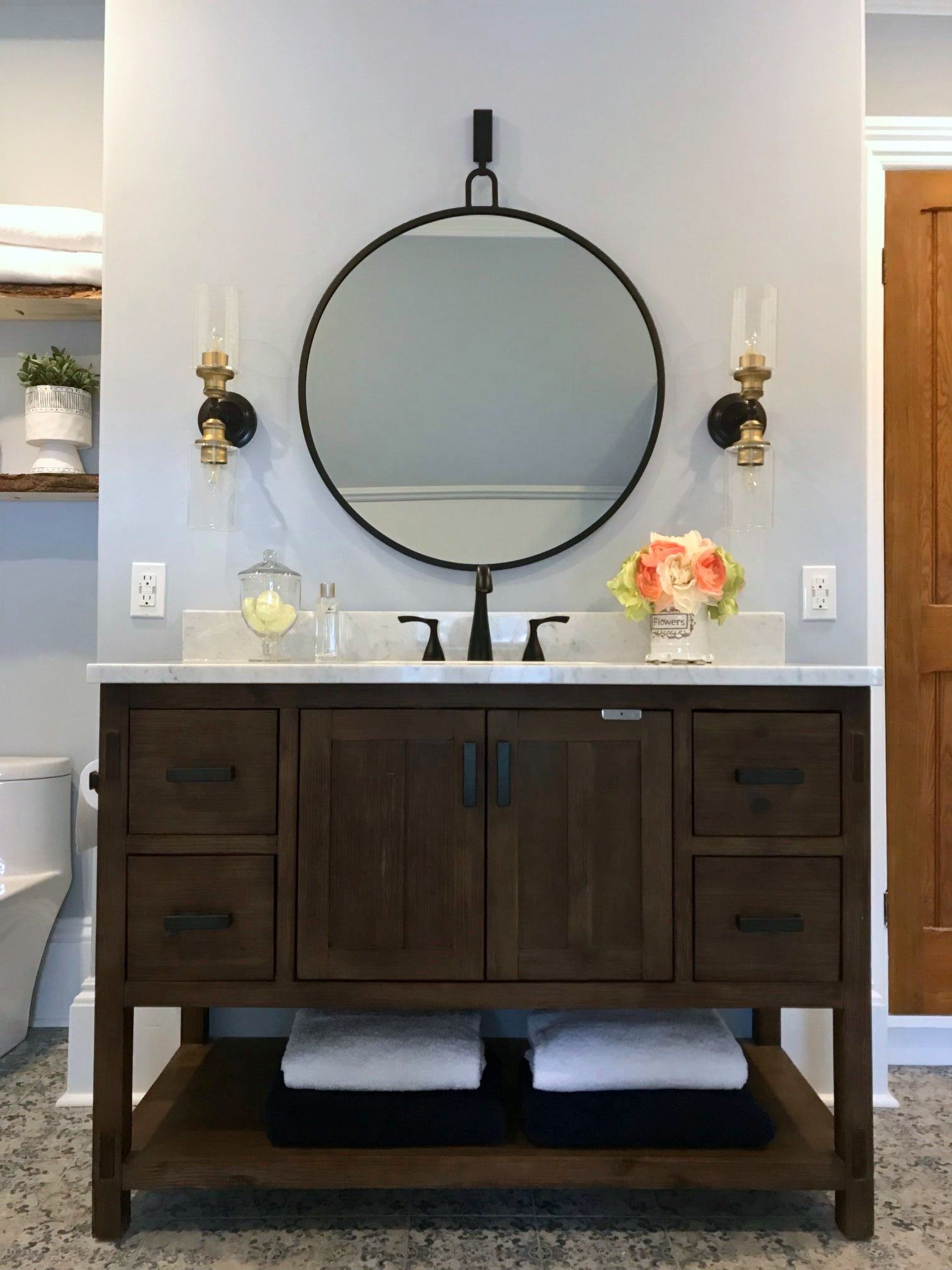 Dark wood vanity with round mirror and wall sconces in Kemptville bathroom renovation
