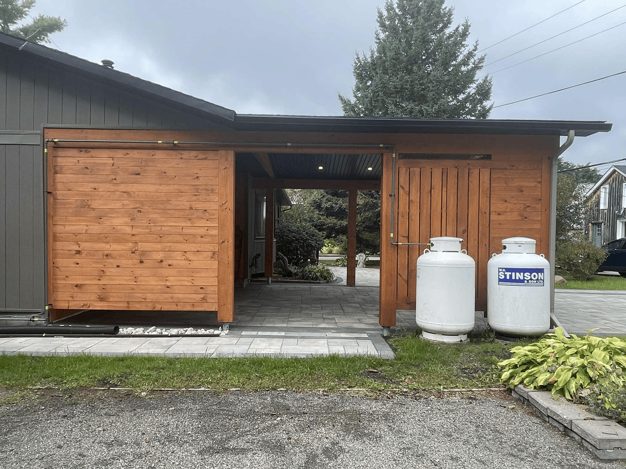 Left exterior view of cedar-clad carport addition with sliding barn-style storage door and stone walkway connection