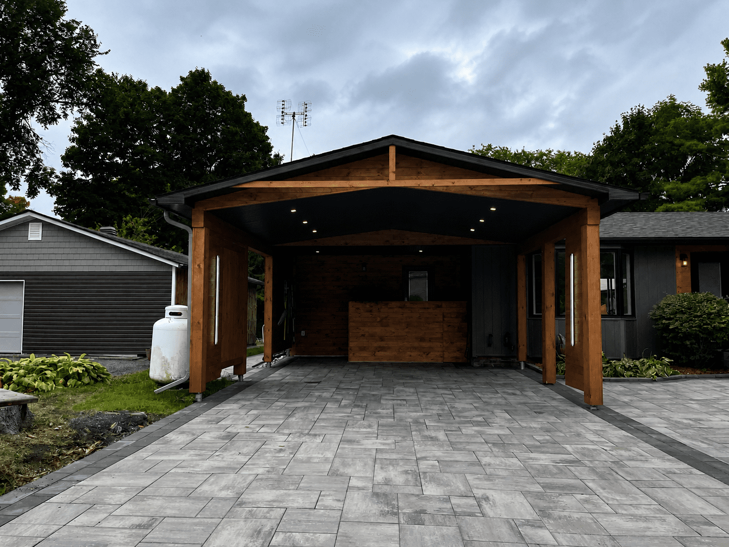 Front view of modern cedar carport addition with integrated storage wall and stone driveway in residential renovation