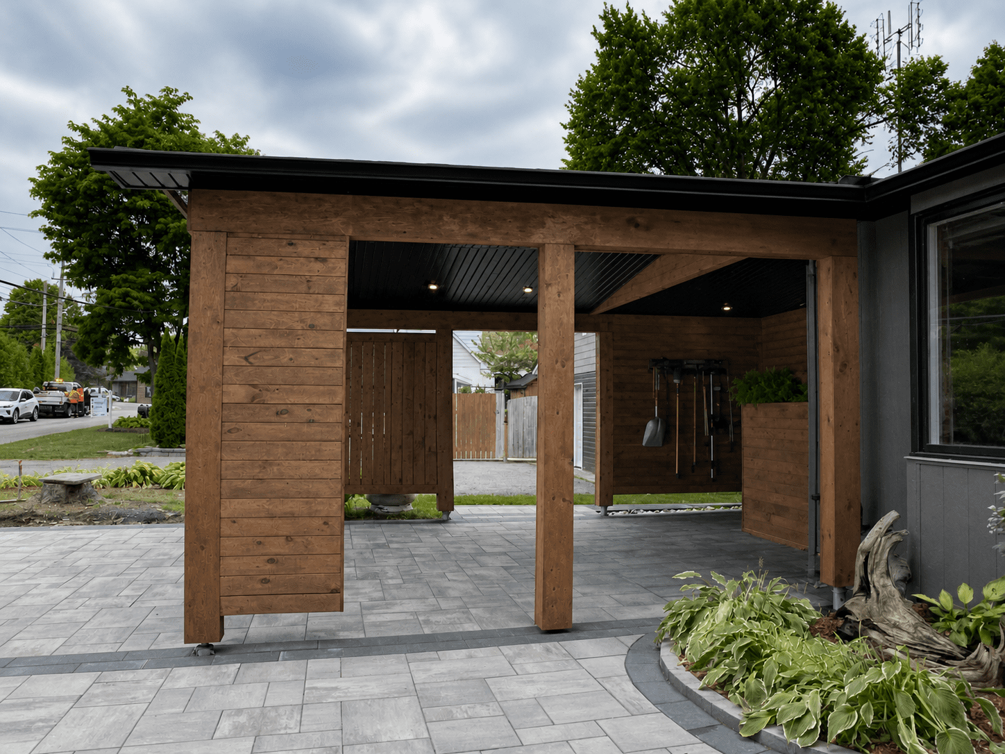Right exterior view of cedar carport addition with timber posts, privacy screen wall, and recessed soffit lighting