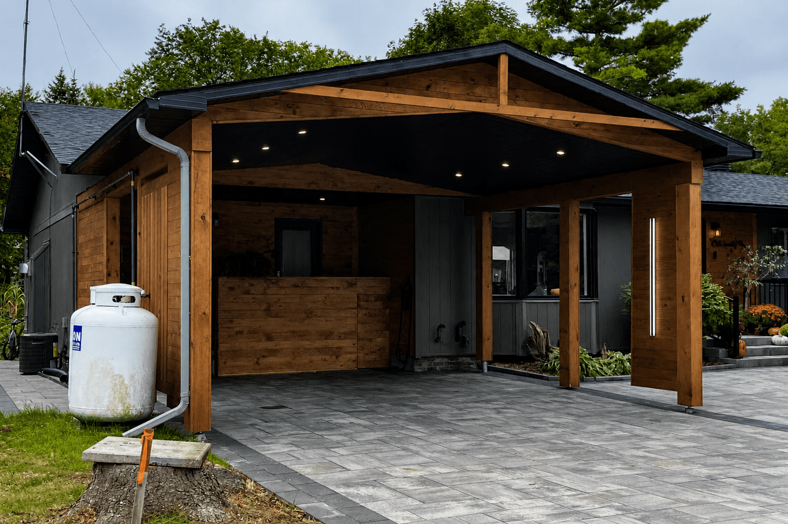 Wide perspective of completed cedar carport addition with timber posts and large-format stone driveway