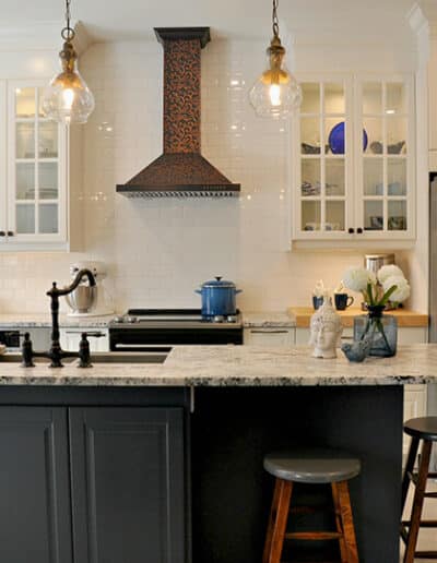 Farmhouse kitchen renovation in Greely with custom range hood, navy island, quartz countertops, and glass-front cabinetry