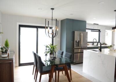Dining room with glass table, modern chandelier, teal cabinetry, and large sliding doors.