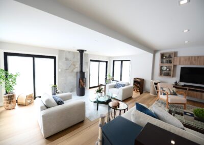 Wide-angle view of living room connected to sunroom with modern seating and wood stove.