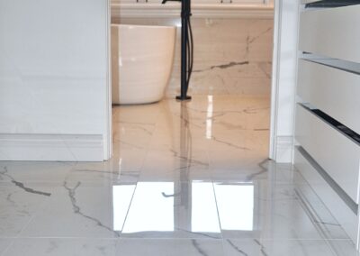 Walk-in closet with polished marble-look tile flooring leading into a modern ensuite bathroom with freestanding tub and black floor-mounted tub filler