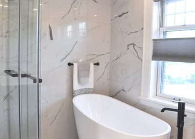 Black and white en-suite bathroom with freestanding tub, marble tile, glass shower, and black tub filler