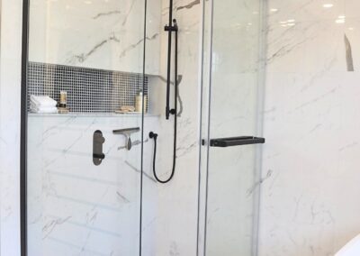 Black and white en-suite walk-in shower with glass enclosure, matte black fixtures, and mosaic tile floor