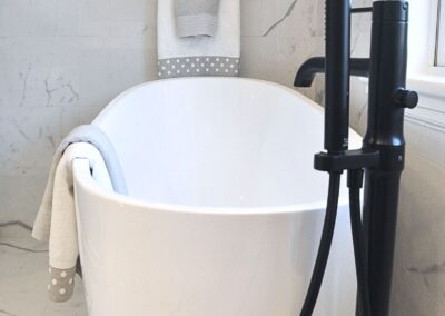 Freestanding white soaking tub with matte black tub filler in a black and white en-suite bathroom