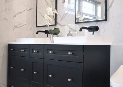 Black double vanity in a black and white en-suite bathroom with wall-mounted faucets and marble tile