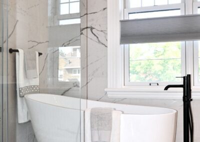 Black and white en-suite bathroom with freestanding tub, glass shower partition, marble tile, and black tub filler