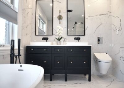 Black and white en-suite bathroom renovation with black double vanity, marble tile walls, wall-mounted faucets, and freestanding tub