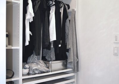 Custom walk-in closet with white built-in cabinetry, drawers, hanging storage, and pendant lighting, with a view into a marble-tiled ensuite bathroom