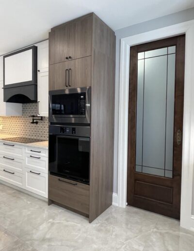 Built-in wall oven with tall wood cabinetry beside frosted glass pocket door