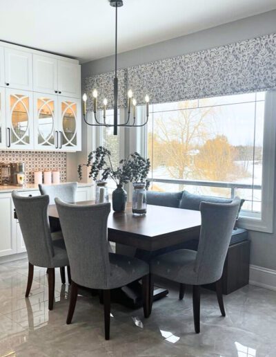 Bright dining area beside white shaker kitchen with large window, glass display cabinets, and contemporary chandelier