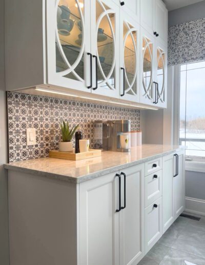 White shaker cabinetry with glass display doors, geometric tile back-splash, and under-cabinet lighting