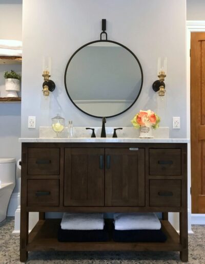 Dark wood vanity with round mirror and wall sconces in Kemptville bathroom renovation