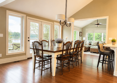 Before photo of a White Lake dining area with a long farmhouse-style dining table, neutral walls, large windows, and an open-concept connection to the kitchen and sun room.