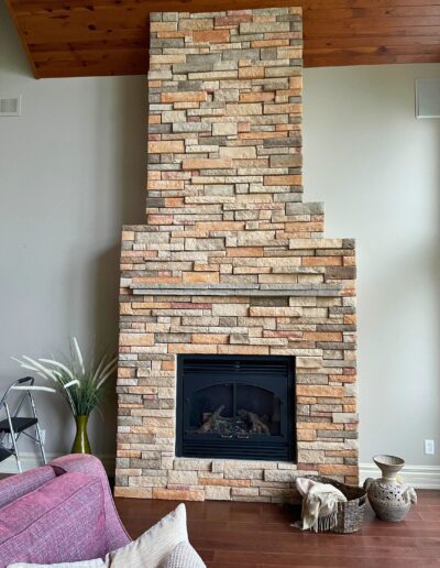 Original White Lake great room fireplace with light stacked stone surround, dark wood floors, and minimal furnishings before redesign.