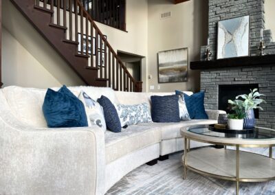 Modern White Lake great room featuring a curved cream sofa, blue accent pillows, dark stone fireplace, and contemporary lakeside styling.