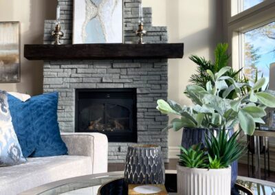 Modern White Lake living room featuring a dark stacked-stone fireplace, wood mantel, cream sofa, blue accent pillows, and contemporary coffee table styling.