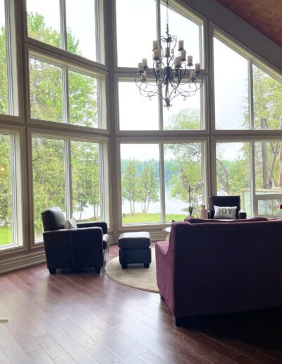 Original White Lake seating area with large lakeview windows, dark flooring, pink sofas, and minimal styling before renovation.