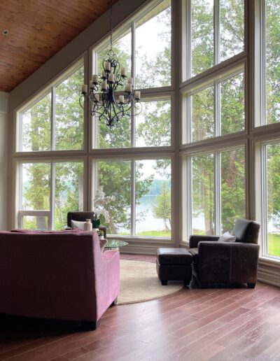 Unfurnished White Lake great room with soaring lakeview windows, dark wood ceiling, pink seating, and open floor space before redesign.