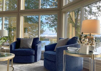 Refined White Lake lounge area with navy swivel chairs, glass side table, oversized windows, and warm natural light.